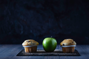 Chocolate chip muffins next to a green apple on a slate plate with a dark background. Copy space. Concept of health in food.