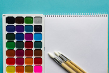 Creative layout with aquarelle palette, paint brushes on blue background. Top view. Artists concept.