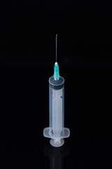 A medical syringe with a needle stands on a white table on a black background. photo for design or advertising