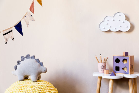 Stylish scandinavian nursery interior with plush dino, design furniture, toys, beautiful decoration and accessories in modern home decor for children room.