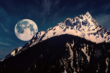 Fullmoon (super moon) sets behind a mountain while the sun comes out.