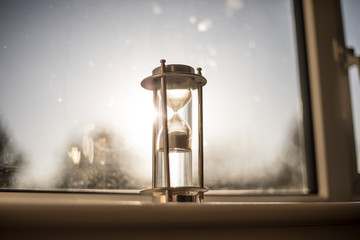 Hour glass on the windowsill with the sun shining through behind it