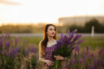 Pretty young woman in a field at sunset. holding flowers