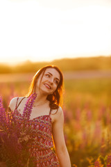 Young girl stand in field overlooking lavender field. Smiling carefree caucasian girl in dress enjoying the sunset