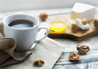 coffee in a white cup on a wooden background, in the background honey, nuts and cheese