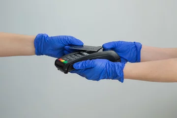 Foto op Plexiglas Woman hand in gloves with credit card swipe through pos terminal and enter pin code. Banking services of electronic money. Financial success and safety. Credit card machine for money transaction. © uflypro