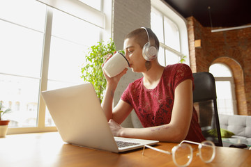 Happy Woman working from home during coronavirus or COVID-19 quarantine, remote office concept. Beautiful bald model, manager doing tasks with laptop, phone, has online conference, meeting.