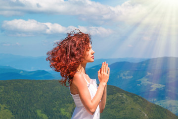 Young beautiful woman praying on top of the mountain with view on valley.