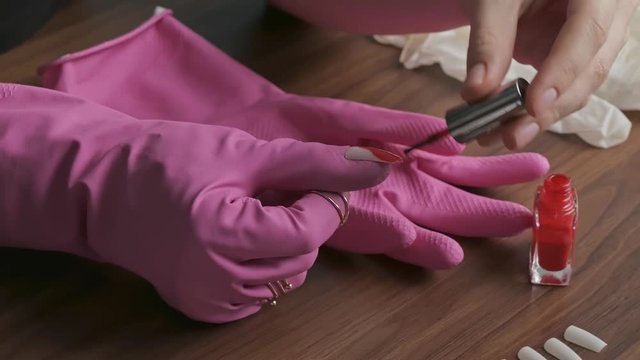 Female hands paint with red varnish false nails glued to a pink rubber glove. Hands of a young woman in gloves with rings. The concept of security and beauty during the quarantine period. Close up.