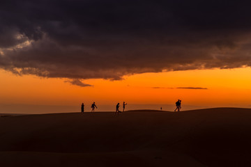 Sand dunes around a city full of people walking down the dunes overlooking the ocean located behind the dunes of Gran Canary island