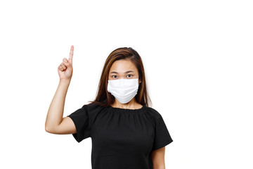 Plain white background. Asian lady with one hand finger pointing upward for text space. asian lady in black shirt. Lady looking straight wearing face mask to avoid spreading of coronavirus.