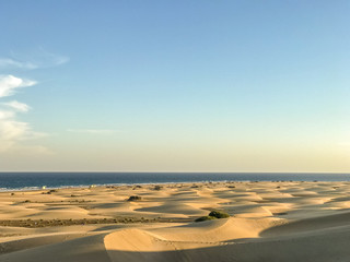 Sand dunes around a city full of people walking down the dunes overlooking the ocean located behind the dunes of Gran Canary island