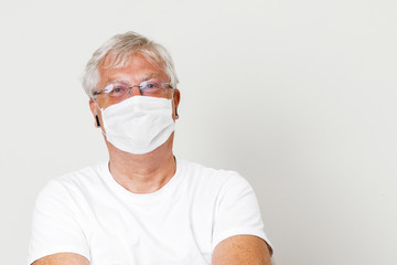 Old British men at risk by coronavirus. Old grey hair guy wearing a face mask for protection against coronavirus. Half body view of man wearing eye glass in paling white background COVID