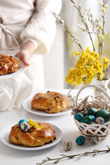 Easter. Palm Sunday. Colored eggs, chicken and quail. Blue, green eggs in white basket. Easter cakes on white plates with the hands of the hostess.  Willow and mimosa in a white vase. Background image