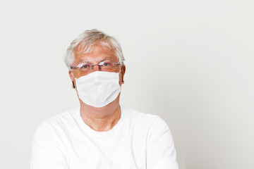 British doctor wearing a face mask in duty for protection against corona virus. Old man wearing eyeglass with grey hair in a white plain background with space for text.