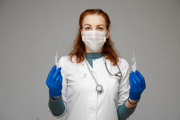 Stock photo portrait of a red-haired scientist in white coat, blue gloves and aseptic mask holding two syringes with treatment from coronavirus infection novel coronavirus disease 2019,COVID-19,nCoV