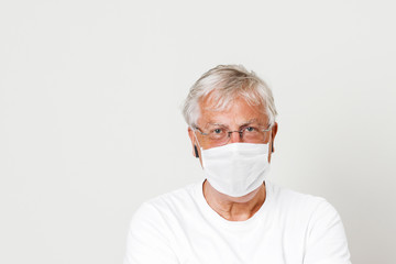 Old British guy at risk by coronavirus. Old grey hair guy wearing a face mask for protection against corona virus. Half body view of man wearing eye glass in paling white background with space