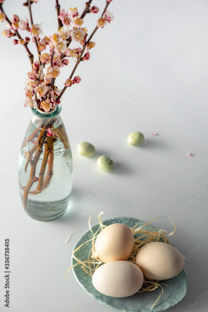 Wall mural Easter composition with flowering pink cherry branch in vase on white background. Easter holiday spring concept .Traditional decor. Greeting card.