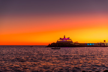 Obraz premium Sunset over the lagoon of orange-red clouds on the horizon and reflections of lights reflecting on sea level with urban area Grand Canary Island Valle
