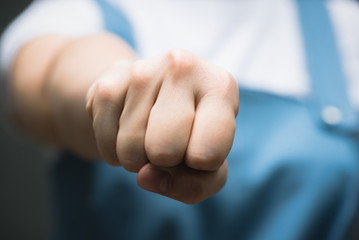 Angry woman in blue dress is shaking her fist close up on gray background.