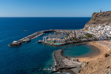 View from the air on the coast and bay in the city of Mogan on the Canary Islands where the bay harbor and people walking along the waterfront inside city