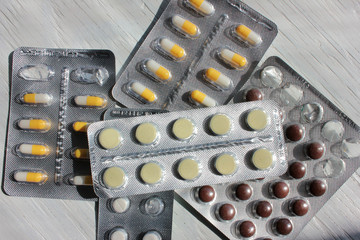 Set of blister packs with pills and capsules on white wooden background
