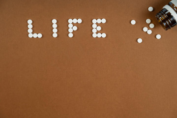 Fototapeta na wymiar The word LIFE written with white pills on brown background. Coronavirus concept. Top view. Space for text