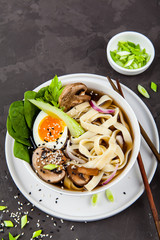 Traditional asian noodle soup pho in bowl, garnished with egg, mushrooms on concrete background. Asian food concept.