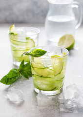 Summer homemade lemonade made from lime, lemon, cucumber and basil with ice in glass on an old concrete background. Selective focus.