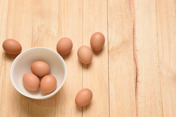 Three eggs and white cup on wooden background, top view and copy space for text