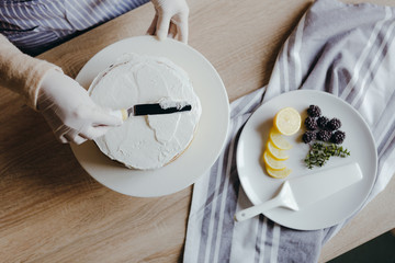 Top view of ousewife in the kitchen cooking a lemon cake with fruits, blackberry, lemon and mint on during quarantine. Recipe of homemade lemon cake. Concept of cooking at home.