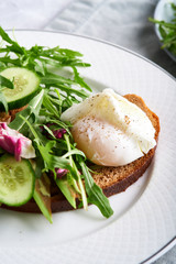 Poached eggs with herbs, avocado and cucumber served on a plate on a light background Copy space