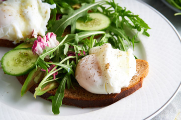Poached eggs with herbs, avocado and cucumber served on a plate on a light background Copy space