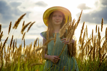 red-haired girl with freckles holds wildflowers in a wheat field
