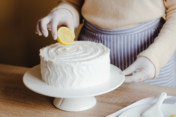 Housewife in the kitchen decorates a lemon cake with fruits, blackberry, lemon, mint during quarantine. Recipe of organic homemade lemon cake. Concept of cooking at home