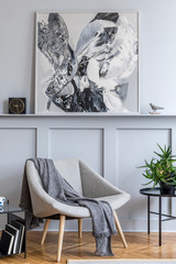 Stylish interior of living room with design grey armchair, pillows, coffee table, paintings, plant, decoration, black clock and elegant personal accessories in modern home decor.