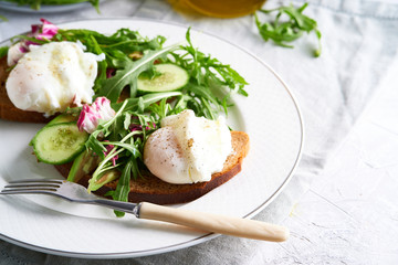 Poached eggs with herbs, avocado and cucumber served on a plate on a light background Copy space