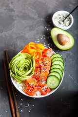 Salmon poke with avocado, cucumber, and rice on dark background , top view. Asian trendy food