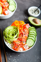 Salmon poke with avocado, cucumber, and rice on dark background , top view. Asian trendy food