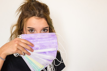 Beautiful brown-eyed girl keeps lot of coloured hygienic masks in hand.