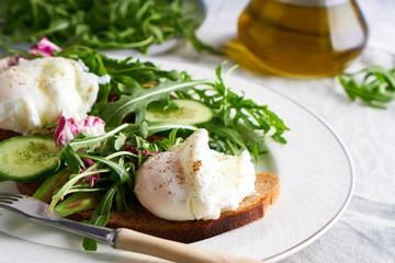 Poached eggs with herbs, avocado and cucumber served on a plate on a light background Copy space