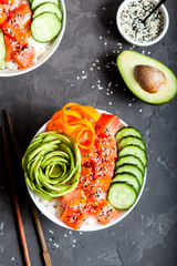 Salmon poke with avocado, cucumber, and rice on dark background , top view. Asian trendy food