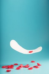 Sanitary pad in flight on a blue background with fallen petals of red flowers. Concept of the beginning of menopause.