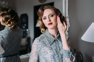 Beautiful blond girl with vintage make up and hairstyle and hand near face staying near mirror