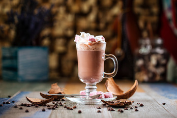 Side view tasty hot cocoa chocolate with whipped cream with marshmallows in a glass mug on a wooden background, horizontal