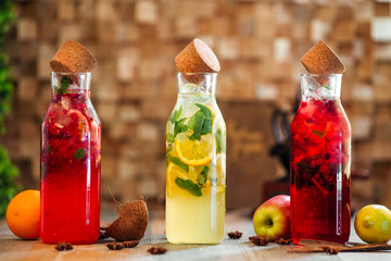 Side view on fresh cool different lemonades set in glass bottle with mint, lemon and berries on the wooden table, horizontal