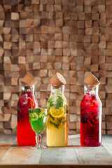 Side view on fresh cool different lemonades set in glass bottle with mint, lemon and berries on the wooden table, vertical