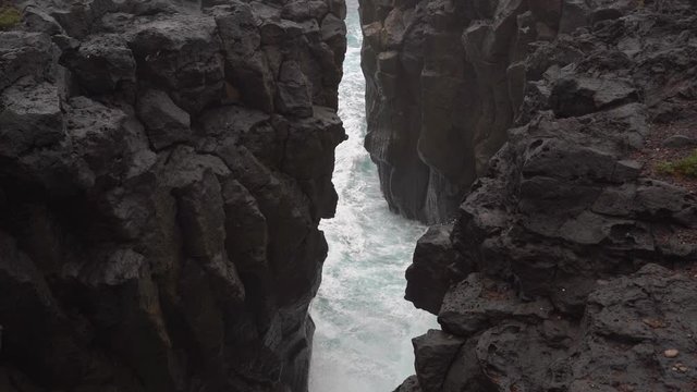 The waves of a rough sea break between the black volcanic rock cliffs on Isla del Hierro on a cloudy winter day.