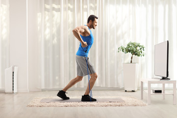 Fit guy with a resistance band exercising at home in front of a tv