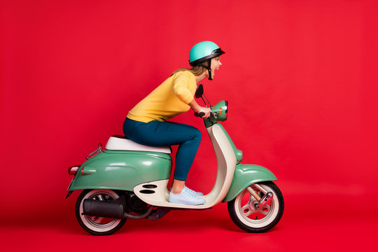 Profile side view portrait of her she nice attractive lovely crazy girlish cheerful cheery girl riding moped having fun adventure isolated on bright vivid shine vibrant red color background